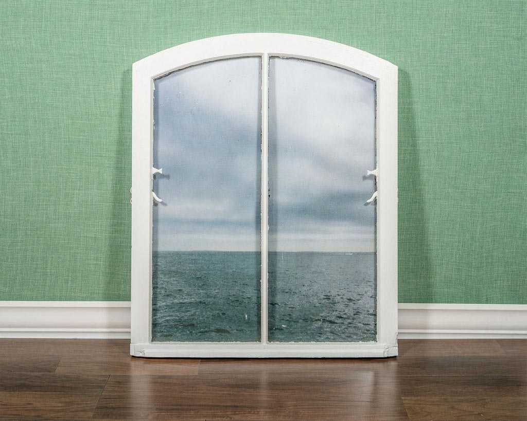 'A white window frame leans up against the wall with a picture of the deep ocean in its panes'