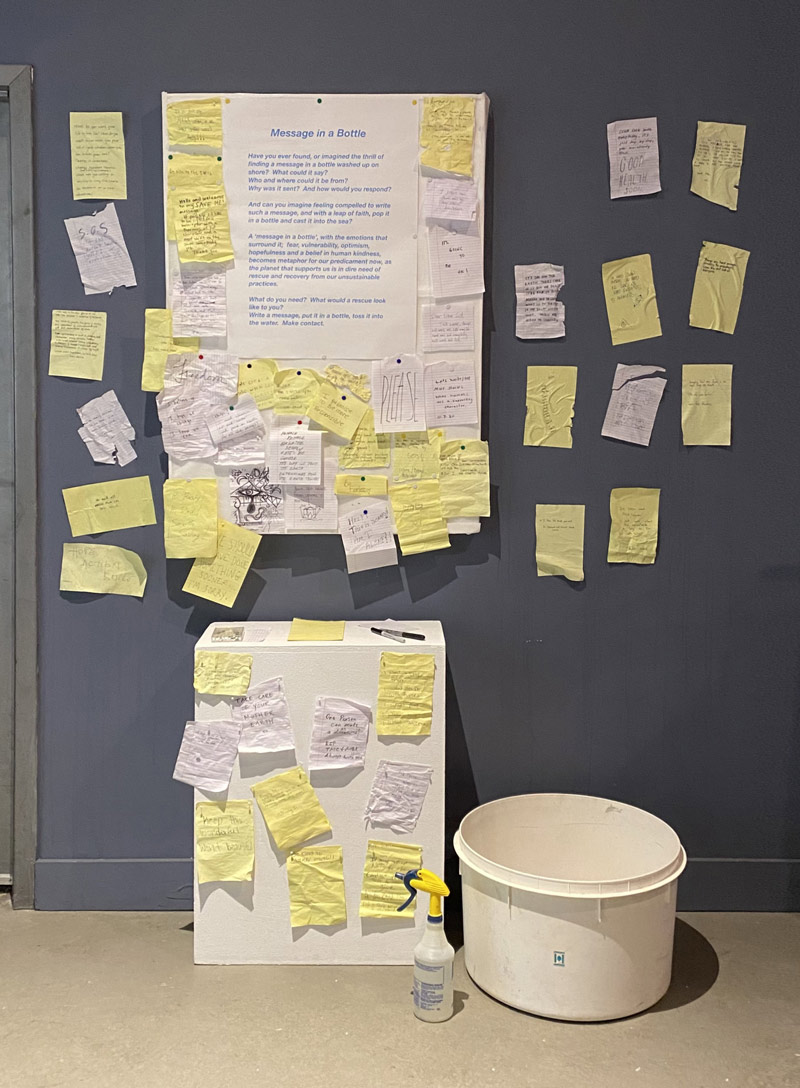 A wall board, podium, and surrounding wall plastered with hand written messages on scraps of note paper of different sizes and colors